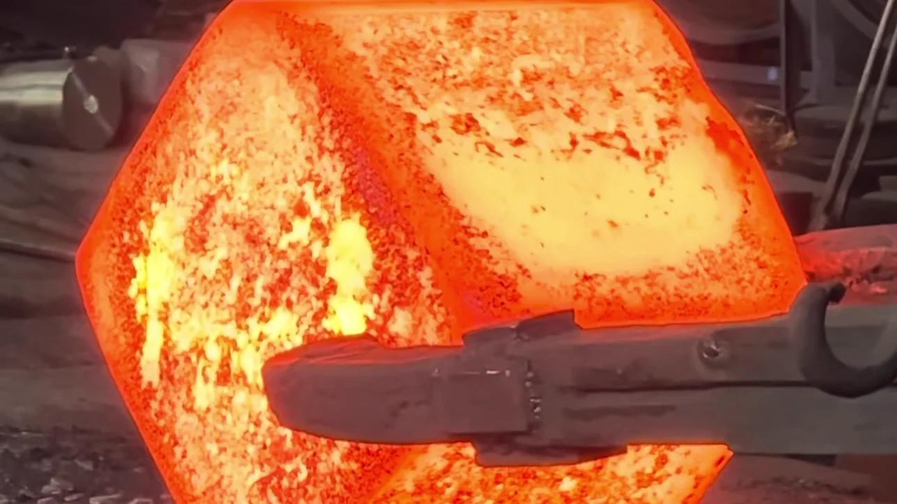 A block of red hot steel held in heavy tongs at a forge